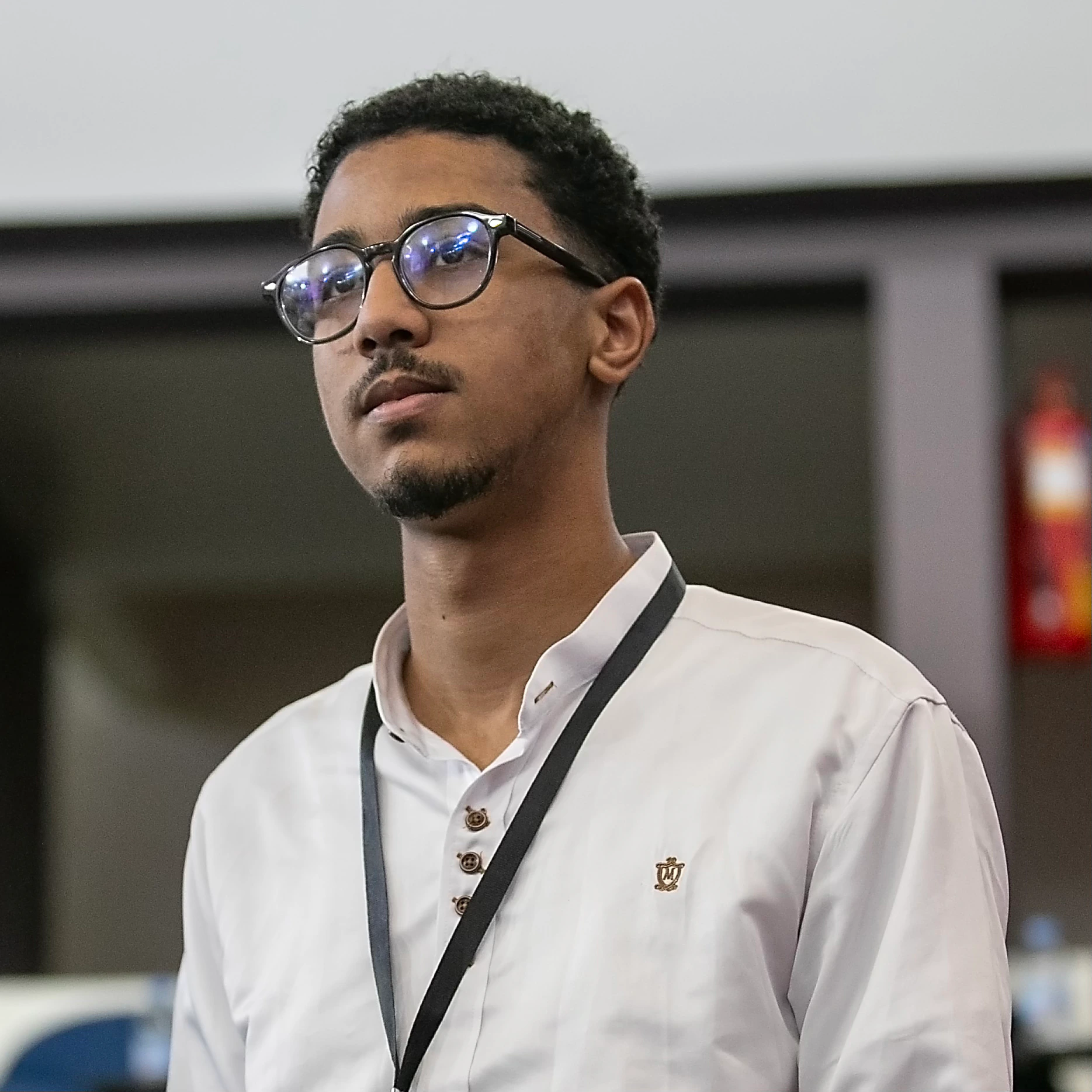 Taha Zizah wearing glasses and a light polo shirt, photographed looking to the side.